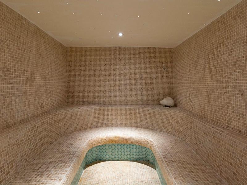 Cozy tiled steam room with curved benches and central water feature under soft lighting.