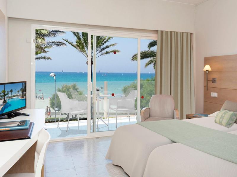 Hotel room with twin beds and sea view through glass doors.