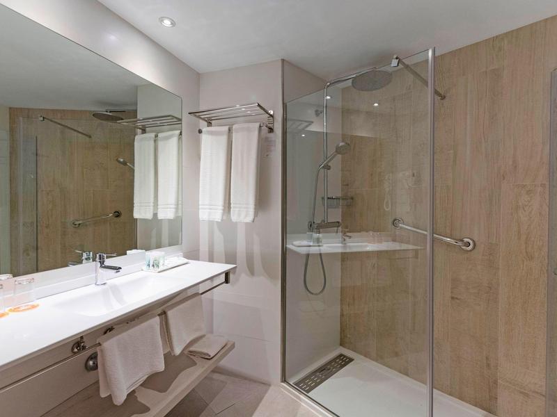 Modern hotel bathroom with glass shower, double sink, and wooden wall panels.