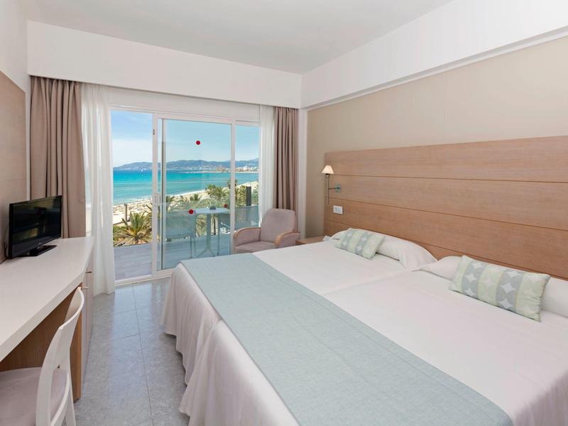 Bright hotel room with sea view balcony, large bed, and pastel decor.
