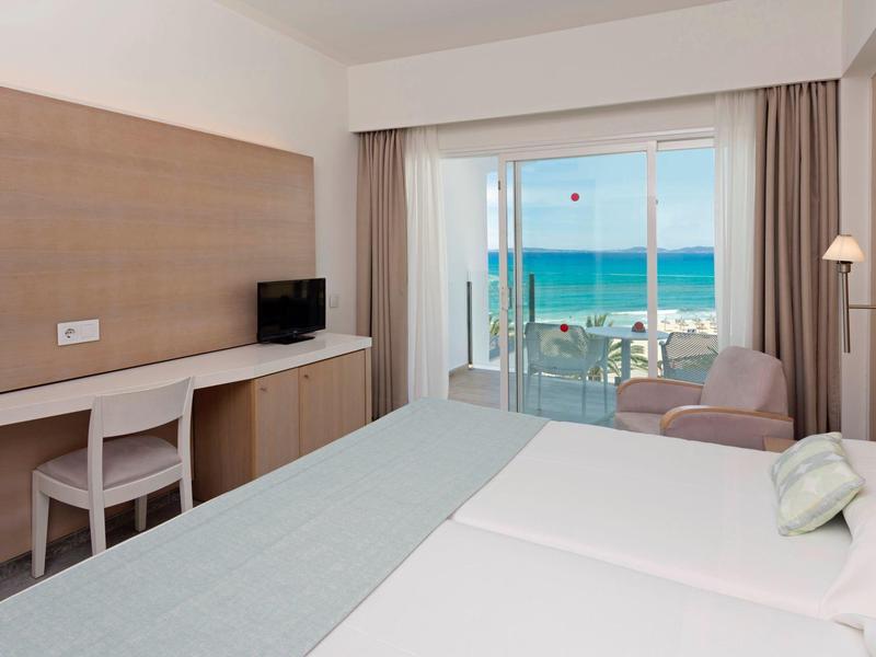 Modern hotel room with twin beds, ocean view balcony, and light wooden furniture.