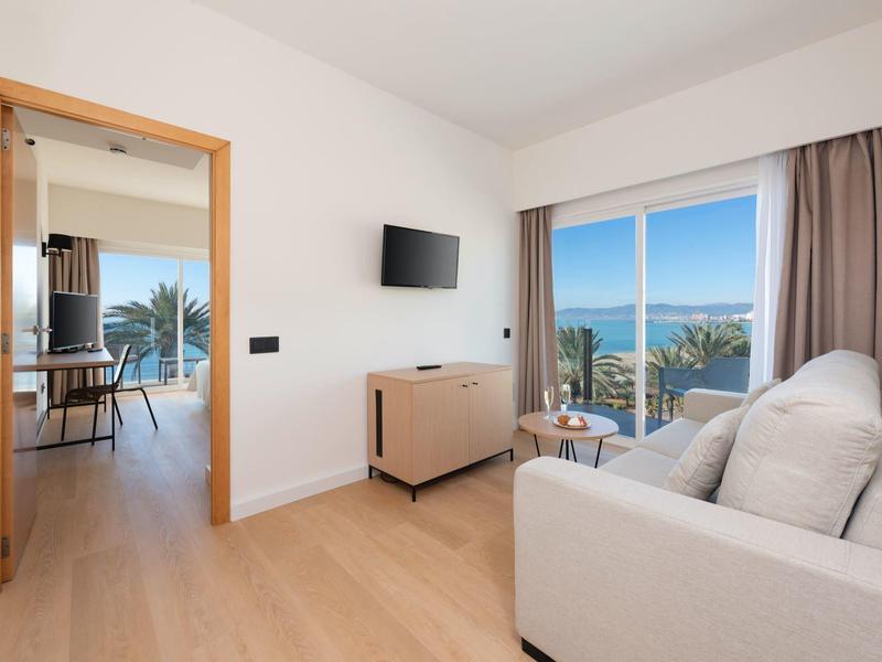 Modern living area with sofa, wall TV, and balcony with sea views in a bright space.