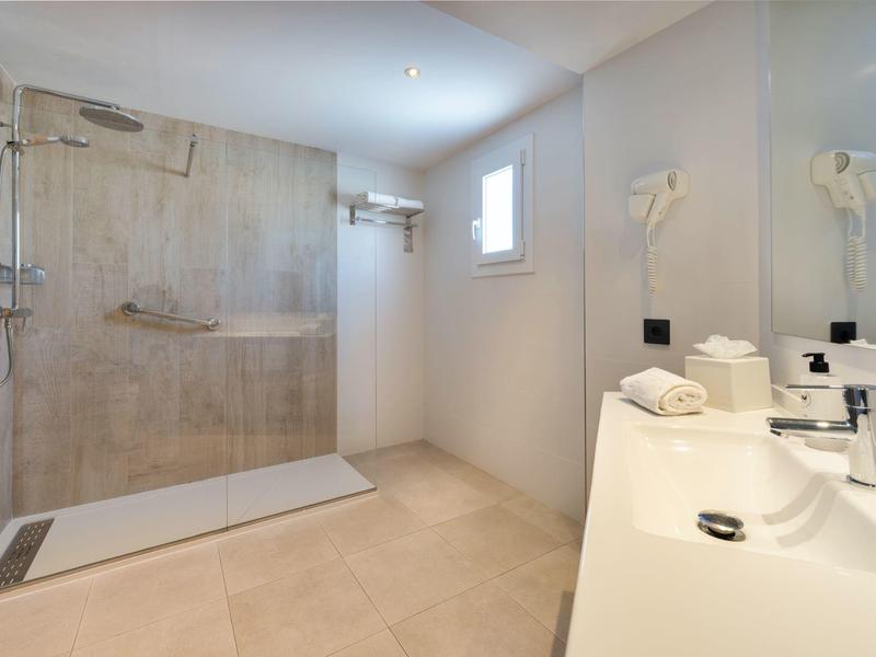 Modern hotel bathroom with walk-in shower, double sink, beige tiles, and natural light.
