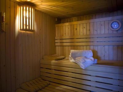 Holzsauna mit Hocker und gefalteten weißen Handtüchern, warmes Licht, Thermometer an der Wand.