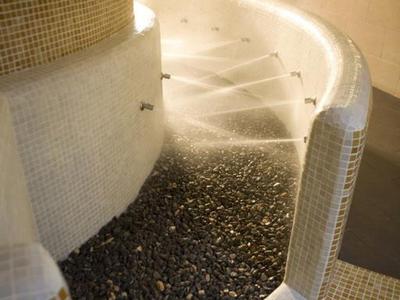 Geschwungene Treppe mit kleinen weißen Fliesen und dunklem Kies am Boden einer modernen Innenraumgestaltung.