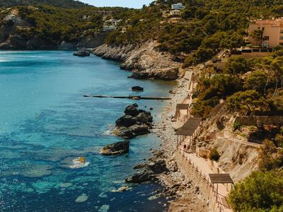 Kleine Badebucht mit steiniger Küste, klarem blauem Wasser und bewaldeten Hügeln im Hintergrund.