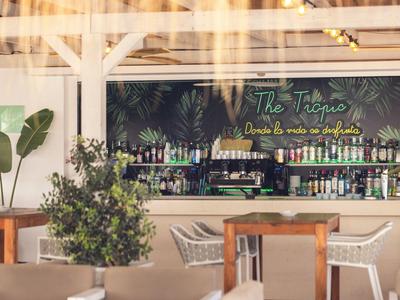 Moderner Hotelbarbereich mit Holzsäulen, Pflanzen und Regalen voller Flaschen.