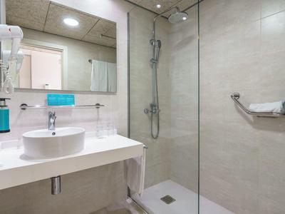 Modernes Badezimmer mit großer Dusche, Waschbecken und hellem Design in einem Hotelzimmer.