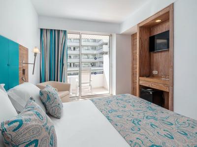 Modernes Hotelzimmer mit großem Bett, Balkon und integriertem Fernseher in Holzverkleidung.