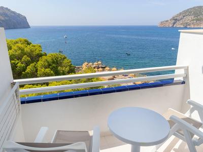 Balkon mit weißem Tisch und Stühlen mit Blick auf das Meer und grüne Hügel.