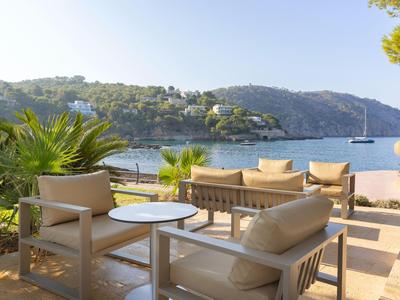 Terrasse mit moderner Sitzgruppe und Blick auf das Meer und Hügel bei klarem Himmel.