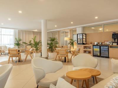 Helle Lounge mit gemütlichen Sesseln, Holztischen und Kaffeemaschine in einem Hotel.