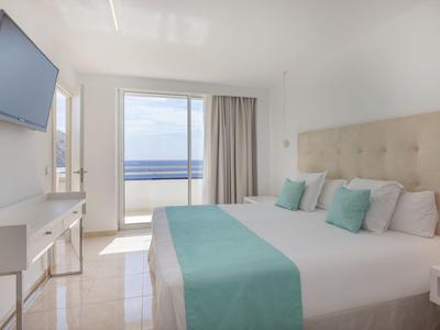 Helles Hotelzimmer mit Meerblick, Doppelbett und modernem Interieur in Weiß und Türkis.