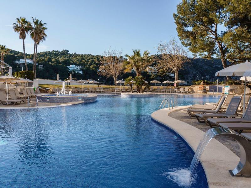 Freizeitpool mit Liegestühlen und Palmen unter klarem Himmel.