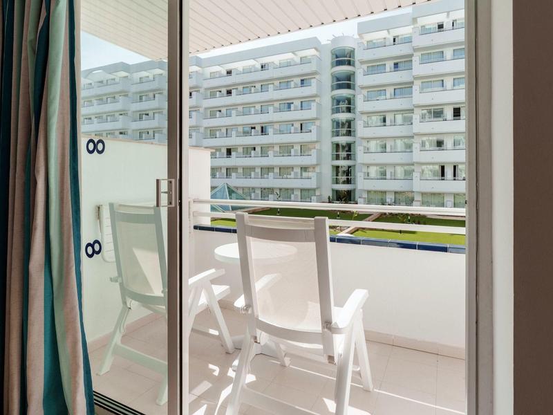 Balkon mit zwei weißen Stühlen und Blick auf benachbartes Wohngebäude.