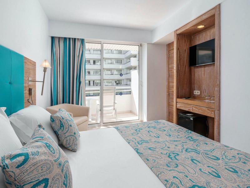 Modernes Hotelzimmer mit großem Bett, Balkon und integriertem Fernseher in Holzverkleidung.