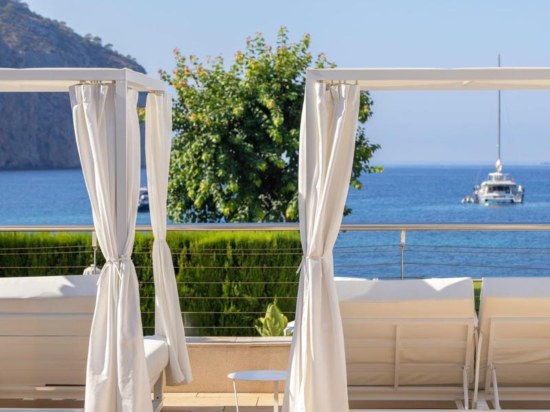 Meerblick mit weißen Vorhängen und Segelboot am Horizont bei klarem Himmel