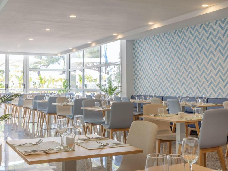 Helles, modernes Restaurant mit Tischen, Stühlen und großem Fenster mit Außenblick.