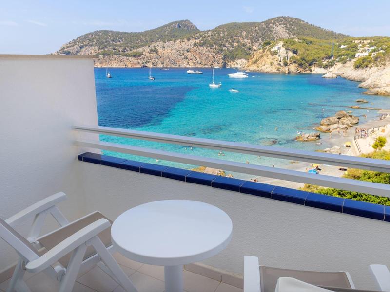 Balkon mit Tisch und Stühlen mit Blick auf das Meer und Hügel im Hintergrund.