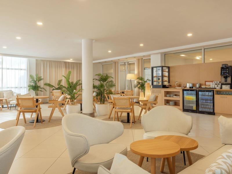 Helle Lounge mit gemütlichen Sesseln, Holztischen und Kaffeemaschine in einem Hotel.