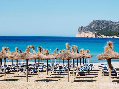 Beach with empty sun loungers under straw roofs and clear blue sea in the background.