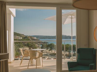 Blick von einem Hotelzimmer mit Balkon auf das Meer und eine sonnige Landschaft.