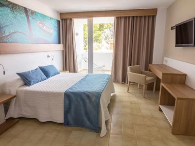 A modern hotel room with double bed, desk, chairs, and balcony windows.