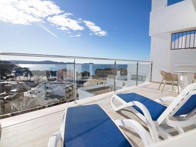 Balcony with blue lounge chairs and glass railing overlooking harbor and sea.