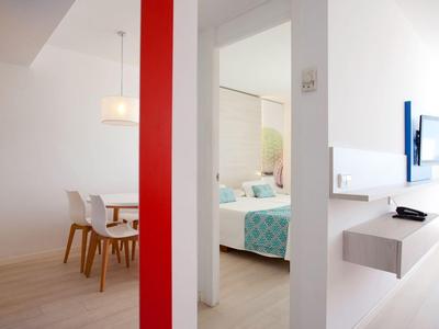 View of a hotel room with dining area and bedroom, white walls and modern design.