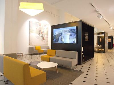 Modern hotel lobby with yellow and gray seating and large digital displays.
