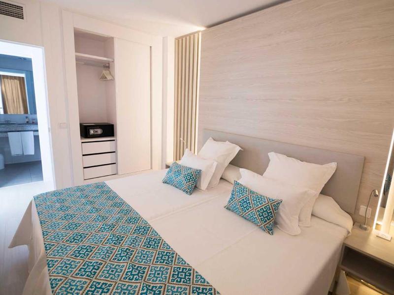 Modern hotel room with double bed, blue and white pillows, and open wardrobe.