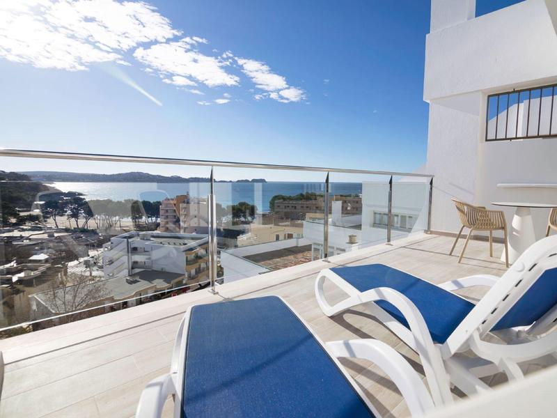 Balcony with blue lounge chairs and glass railing overlooking harbor and sea.