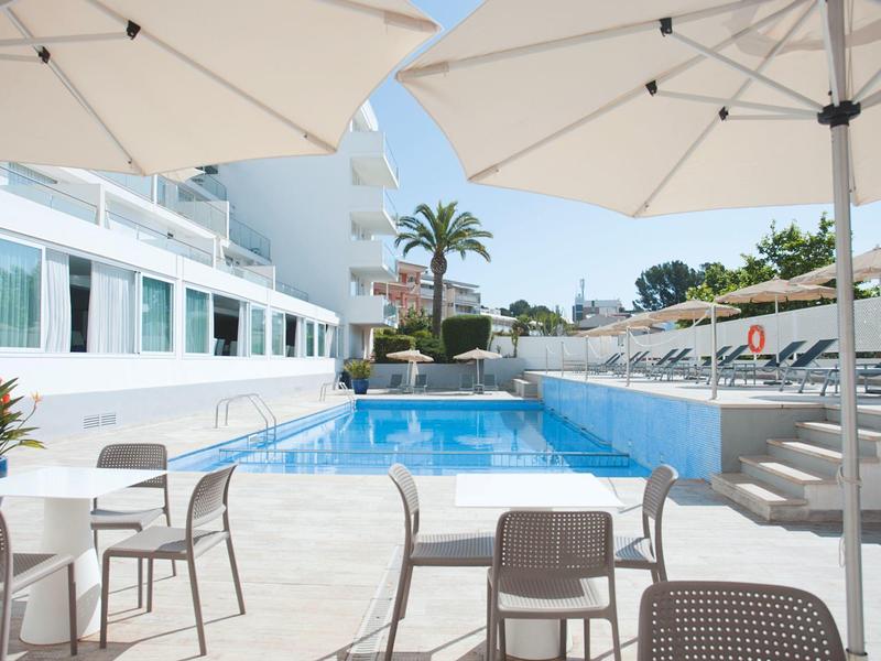 Modern outdoor pool area with umbrellas and chairs next to a hotel building.