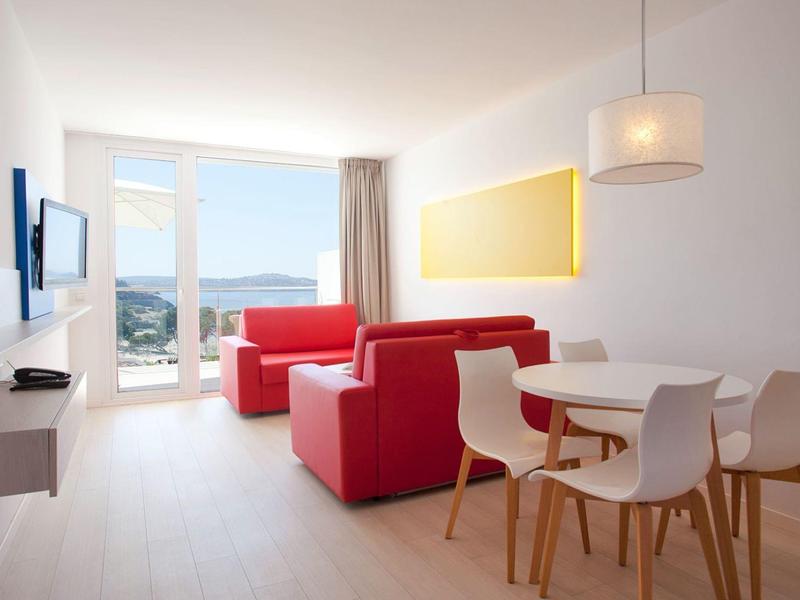 Bright living room with red armchairs, dining table, and view of water and hills.