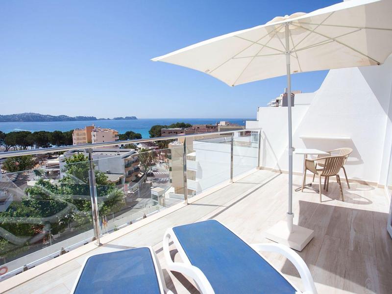 Balcony with lounge chairs and umbrella overlooking the sea and town.