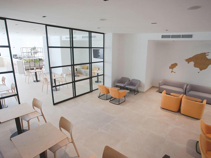 Modern hotel lounge area with seating and glass partitions in a bright room.