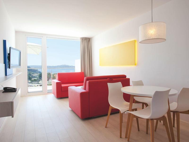 Bright living room with red sofas, dining area, and sea view through large windows.