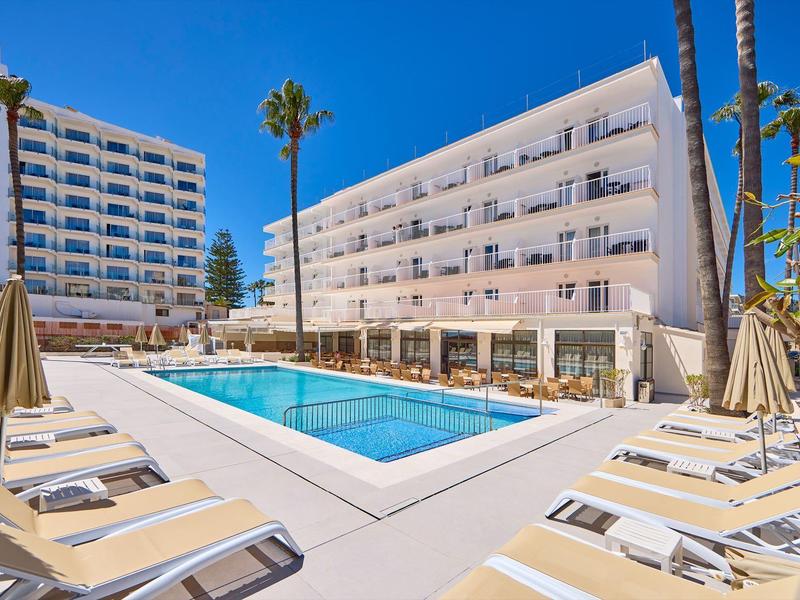 Piscina di hotel moderna con lettini e ombrelloni ombreggiati sotto un cielo azzurro.