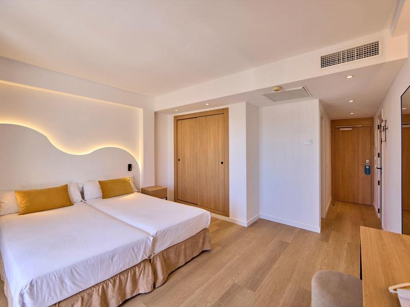 Camera d'hotel luminosa con due letti singoli, pavimento in legno e illuminazione moderna.