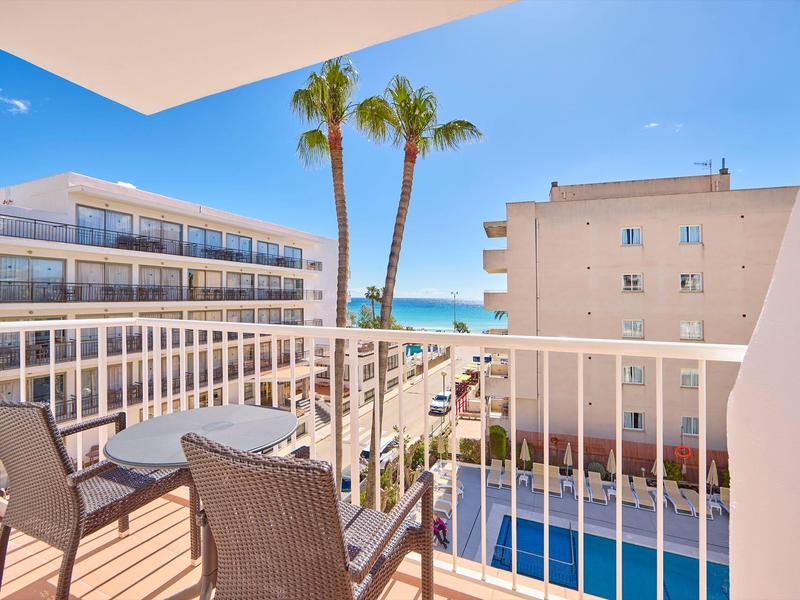 Balcone con tavolo e sedie con vista sulla piscina, edifici e mare sullo sfondo.