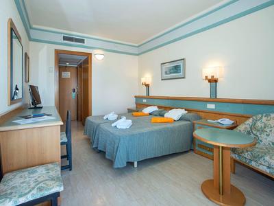 Ein einfaches Hotelzimmer mit zwei Betten, Schreibtisch, Stühlen und sanfter Beleuchtung.