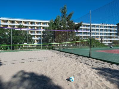 Sandvolleyballfeld neben Tennisplatz mit mehrstöckigem weißen Gebäude im Hintergrund.