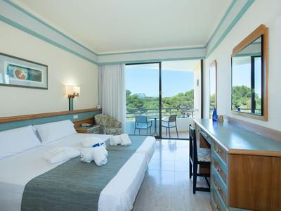 Lichte hotelkamer met bed, balkon en uitzicht op groen landschap.