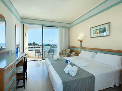 Lichte hotelkamer met tweepersoonsbed en balkon met uitzicht op zee.