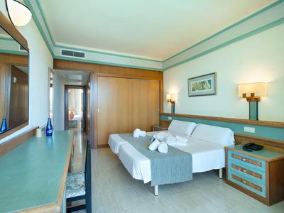 Lichte hotelkamer met tweepersoonsbed, twee nachtkastjes, bureau en grote spiegel.