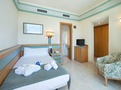 Een eenvoudig ingericht hotelkamer met een eenpersoonsbed, rolstoel en kleine tv.