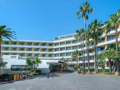 Modern hotel met gebogen wit gebouw, palmbomen ervoor en een helderblauwe lucht.