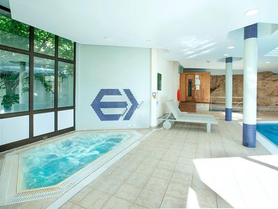 Moderne hotel wellnessruimte met jacuzzi, zwembad en grote ramen met uitzicht op planten.