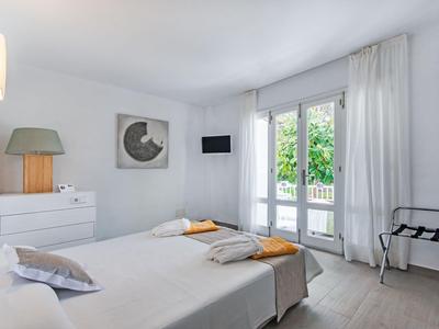 Lichte hotelkamer met tweepersoonsbed, ladekast, fauteuils en balkon met uitzicht op groen.
