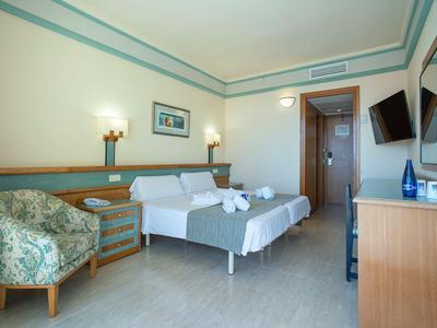 Moderne hotelkamer met tweepersoonsbed, fauteuil, bureau en aan de muur gemonteerde tv.